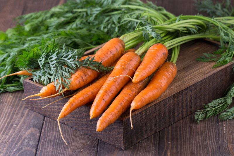 on a dark wooden surface is a wooden board with fresh carrots with leaves still attached