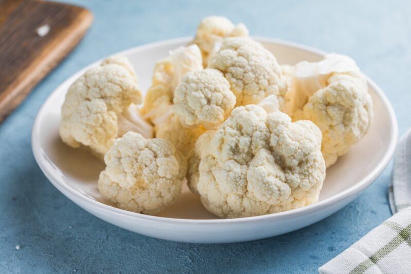 on a blue surface is a white dish with cauliflower florets