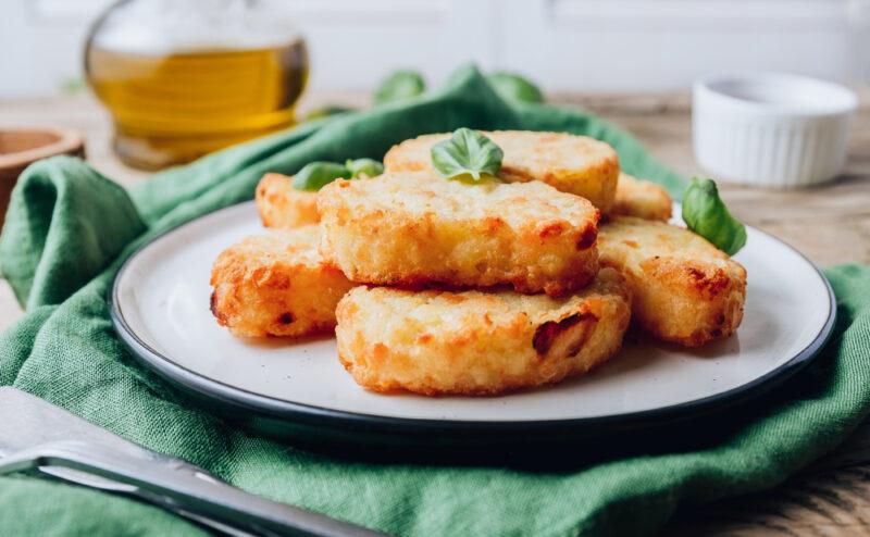 on a wooden surface is a plate with cauliflower has browns with herbs on top, resting on top of a green table napkin