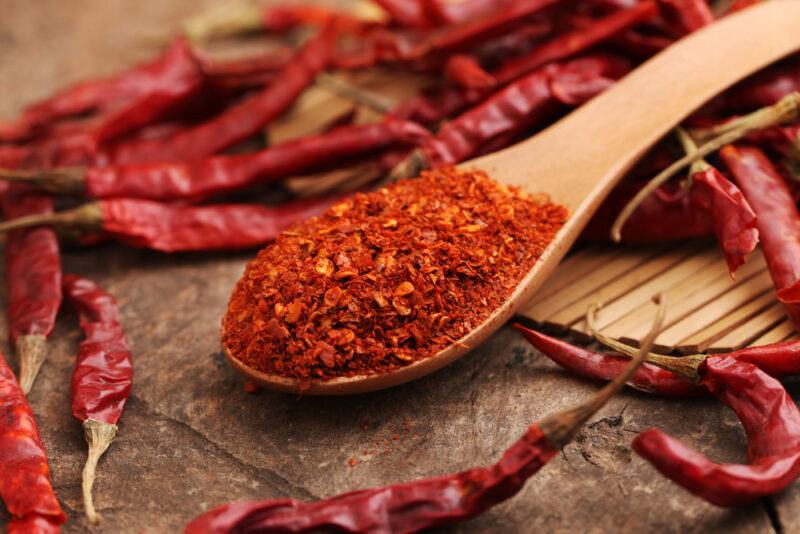 on a wooden surface is a wooden spoon full of cayenne powder with loose dried cayenne peppers around it