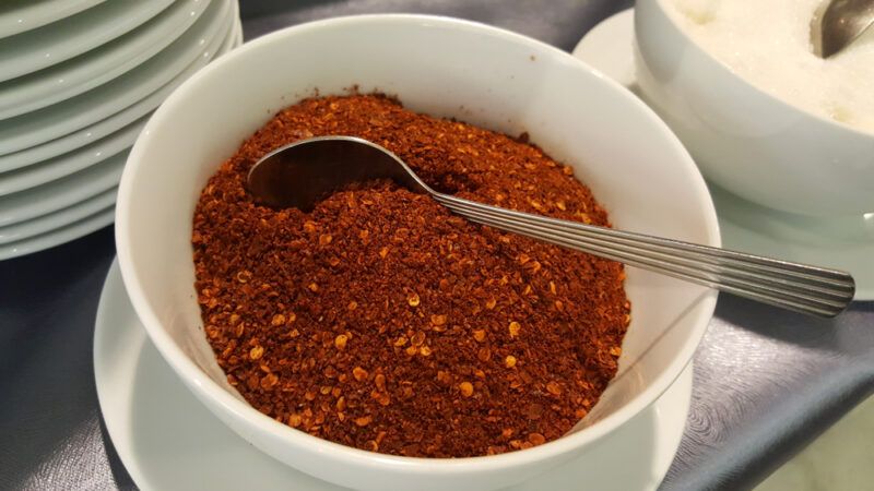 closeup image of a white bowl with cayenne pepper powder with a silver spoon shoved in it, at the back is a pile of white dishes