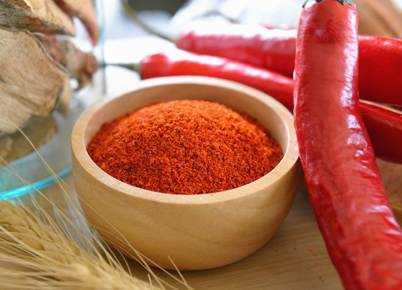 cayenne powder on a wooden bowl with a couple fresh cayenne pepper on the side