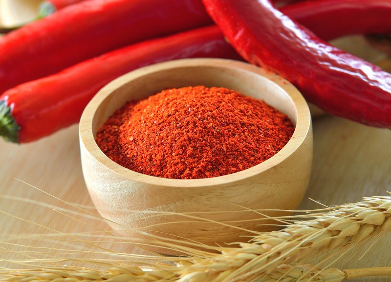 closeup image of a wooden bowl full of cayenne powder with fresh cayenne at the back