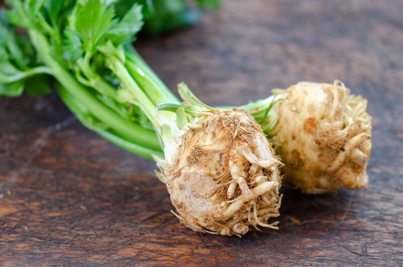 on dark brown surface is a couple of celeriac or celery roots, with the leaves still attached