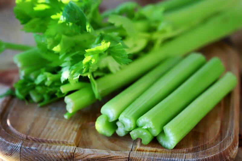 a closeup image of a wooden chopping board with celery stalks on it