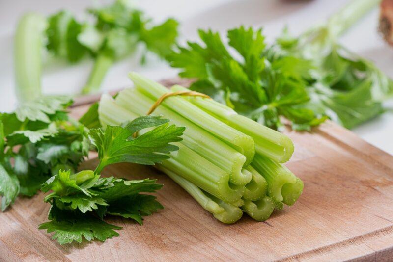 a bunch of celery stalks with celery leaves around it on a wooden chopping board