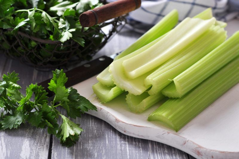 sliced celery sticks on a white plate, with celery stems surrounding it