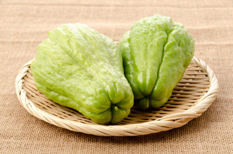 on a burlap is a weaved round tray with a couple of whole chayote