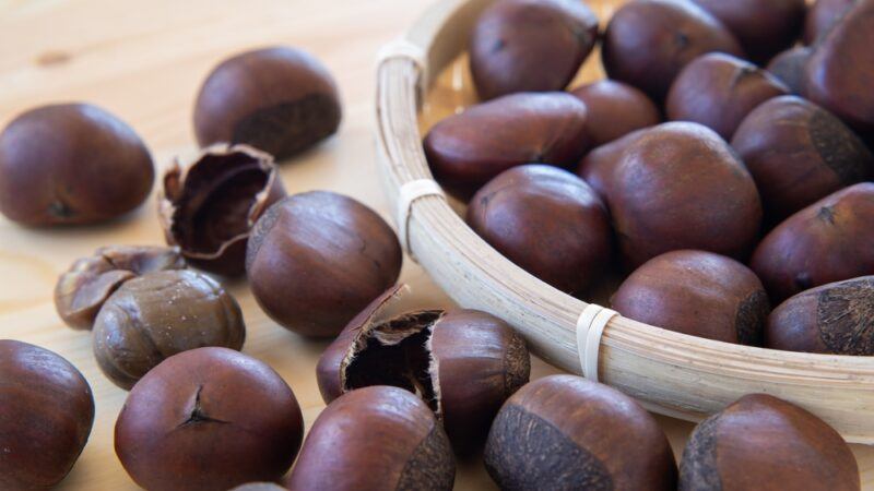 on a wooden surface are loose chestnuts with a partial image of a weaved tray with chestnuts