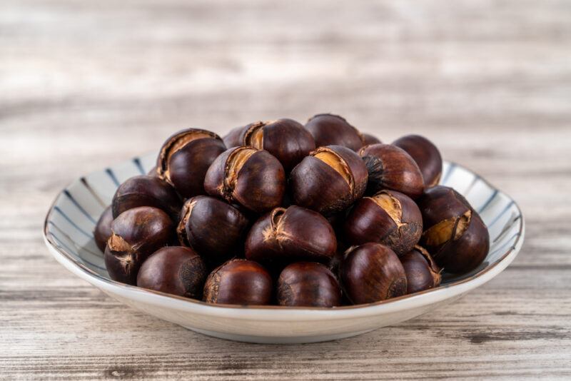 on a wooden surface is a dish full of chestnuts