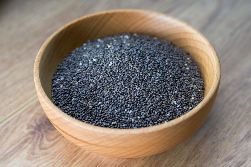 on a wooden surface is a wooden bowl with chia seeds