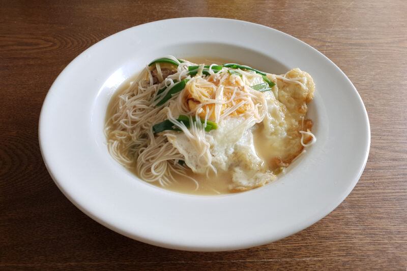 a white dish with misua chicken soup, with fried egg toppings and some greens