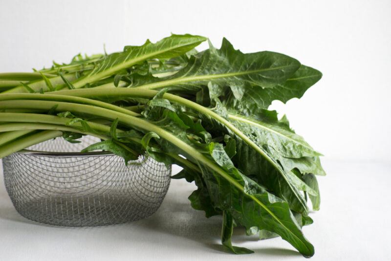 on a white surface is a metal colander with chicory greens