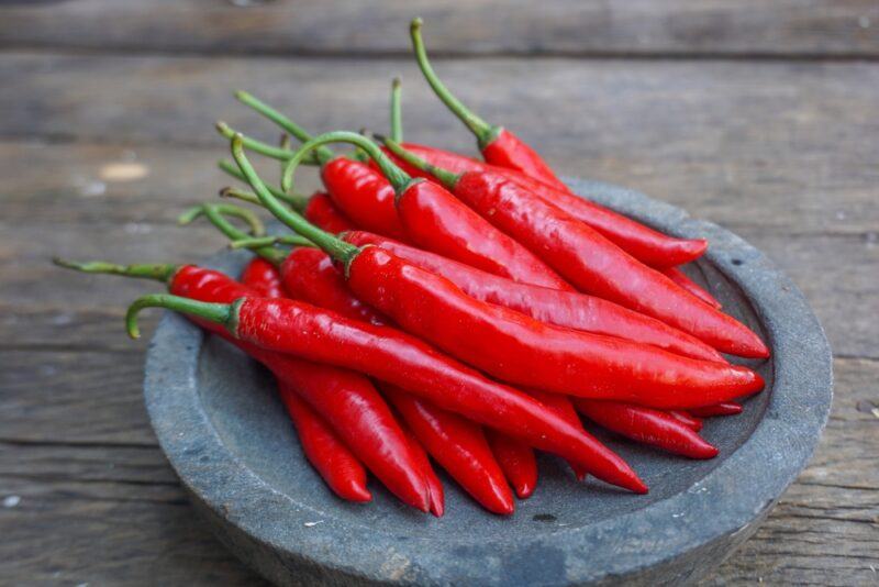 on a wooden surface is a stone dish full of fresh chili peppers