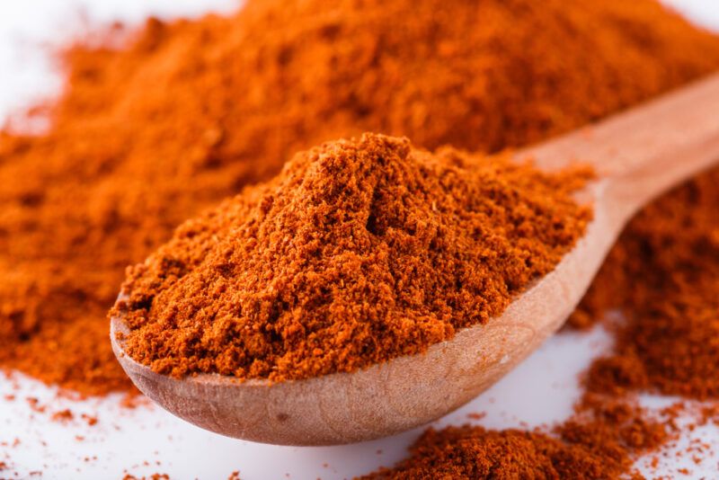 a closeup image of a mound of chili powder with a wooden spoon full of chili powder as well