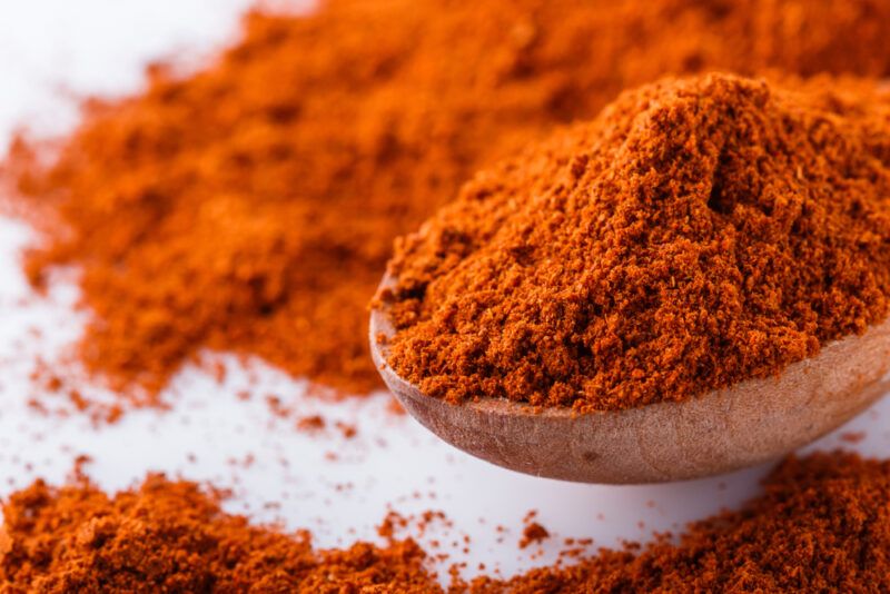 on a white surface is a closeup up image of a wooden spoon full of chili powder on a small mound of chili powder