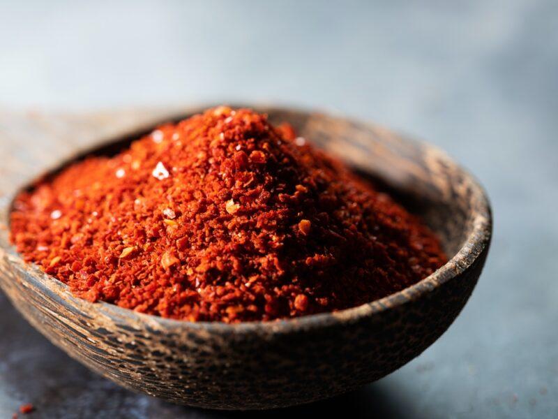 on a dark-colored concrete surface is a closeup image of a wooden ladle full of chili powder