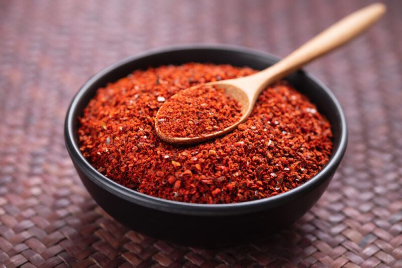 on a weaved brown placemat is a black wooden bowl full of chili powder with a wooden spoon on top