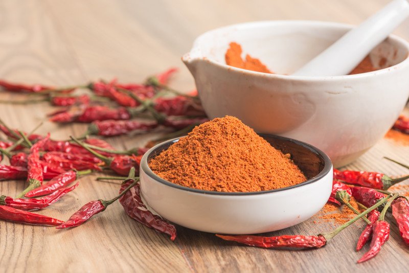 a white bowl full of chili powder with dried chili peppers around it and a white mortar and pestle at the back