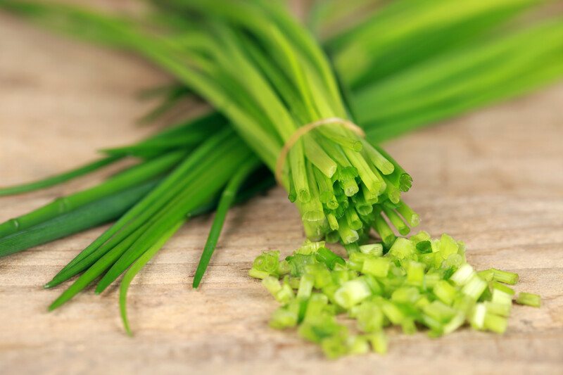 on a wooden surface is a closeup image of a couple of bundles of fresh chives, with one of the bundle partially minced