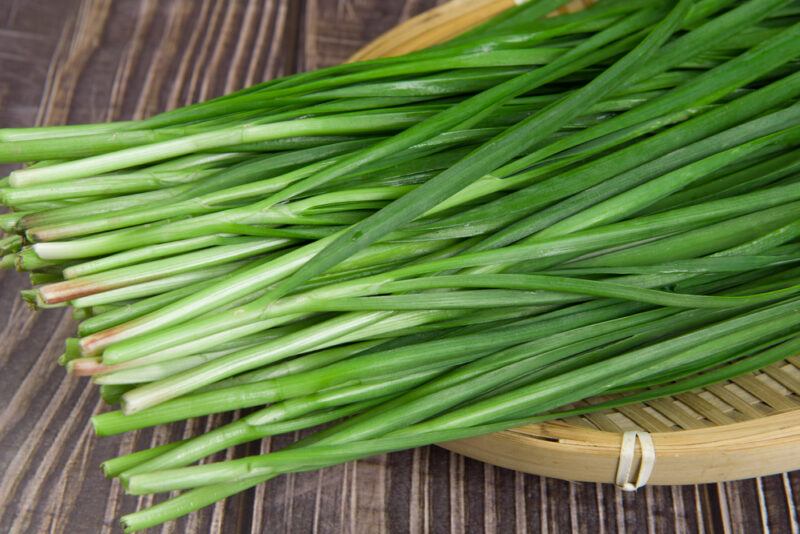 on a wooden surface is a weaved round shallow tray with fresh chives