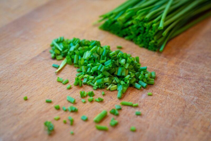 a closeup image of a wooden chopping board with a bunch of partially minced chives