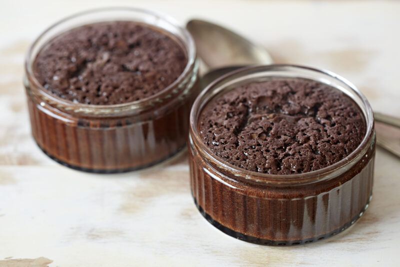 a couple of chocolate pudding cakes in ramekins with a silver dessert spoon beside it