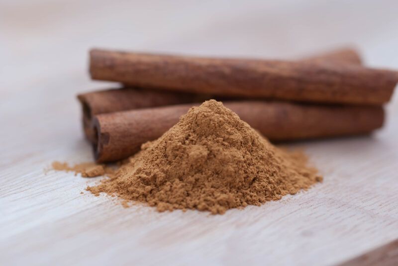 on a wooden surface is a mound of ground cinnamon with a pile of cinnamon sticks behind it