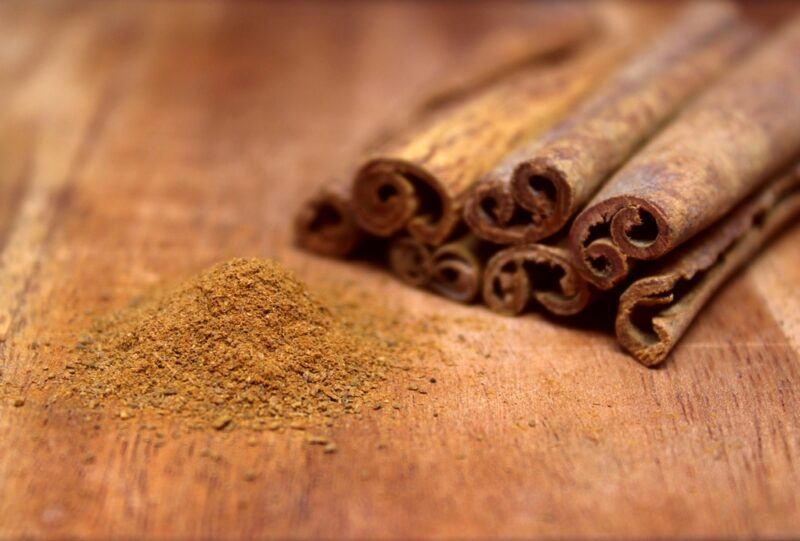 on a wooden surface is a small mound of ground cinnamon with a few cinnamon sticks behind it