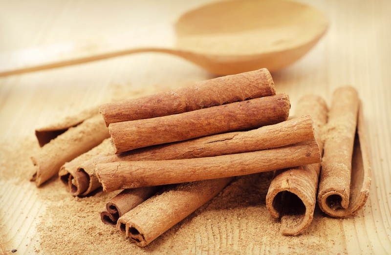 closeup image of a pile of cinnamon sticks on a wooden surface with wooden ladle at the back