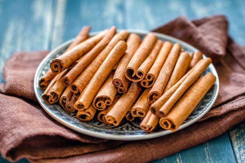 cinnamon sticks on a printed plate resting on a rust-colored table cloth on a rustic-looking blue wooden surface