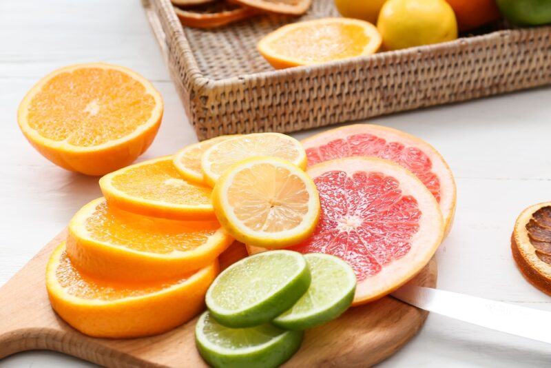 on a wooden chopping board are round slices of different citrus, at the back is a partial image of a woven tray with sliced citrus as well