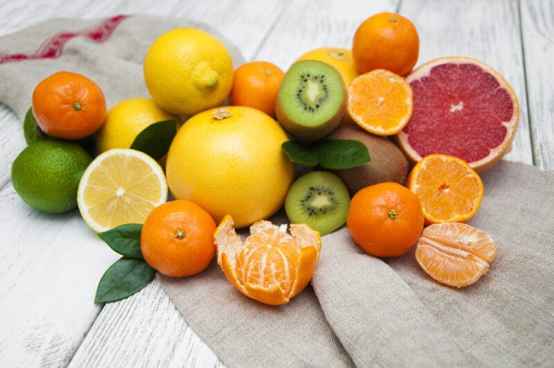 on a rustic looking white wooden surface is a spread of different kinds of citrus fruits partially lying on top of a grey-colored table napkin