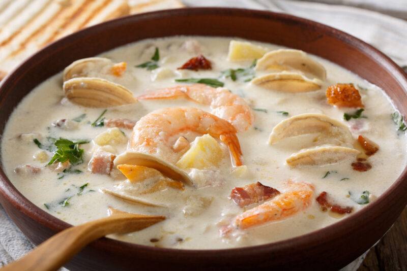 closeup image of a brown ceramic bowl full of clam chowder with a wooden spoon in it