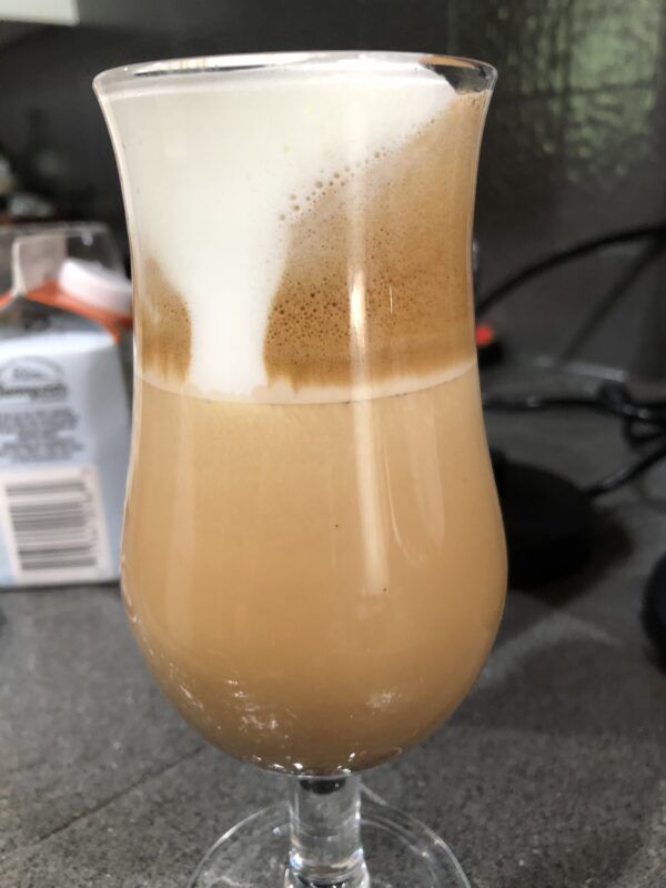 closeup of thick milk foam in curved glass with espresso