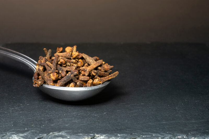 on a concrete surface is a closeup image of a metal spoon full of cloves