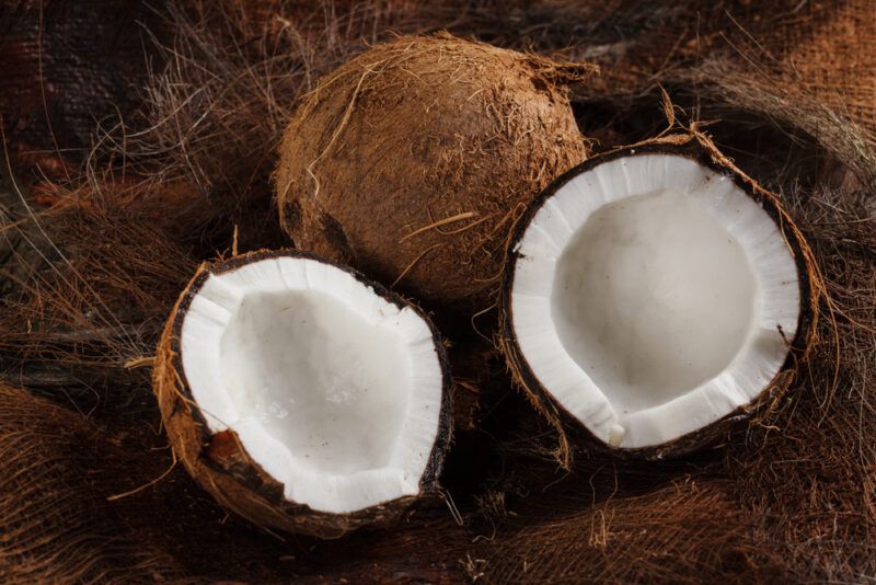 on a dark wooden surface are a couple of coconuts with one cut in half with its white meat showing