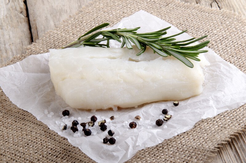 fresh cod on a white parchment paper with fresh thyme on top and loose black peppercorns and salt, resting on a burlap cloth