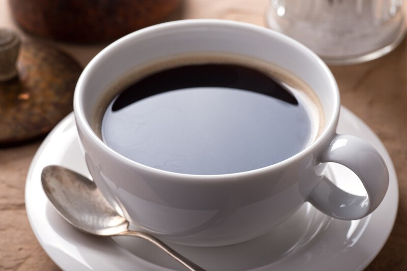 closeup image of a white cup and saucer with black coffee in it