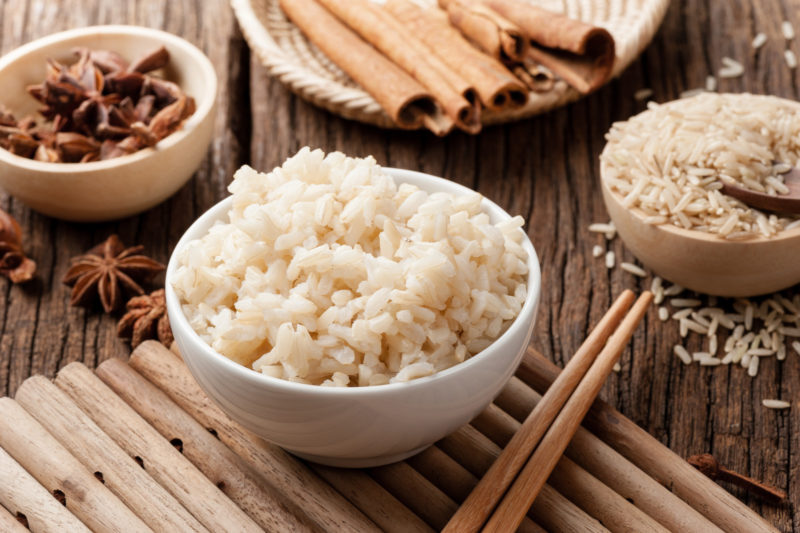 cooked brown rice on a white bowl | Food For Net Bowl of brown rice, chopsticks, star anise and cinnamon barks.