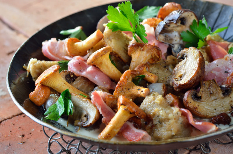 cooked champignon mushrooms on a black plate | Food For Net a plate of cooked chantarellemuschrooms with bacon.