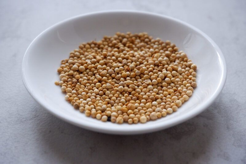 on a concrete surface is a white dish with whole coriander seeds