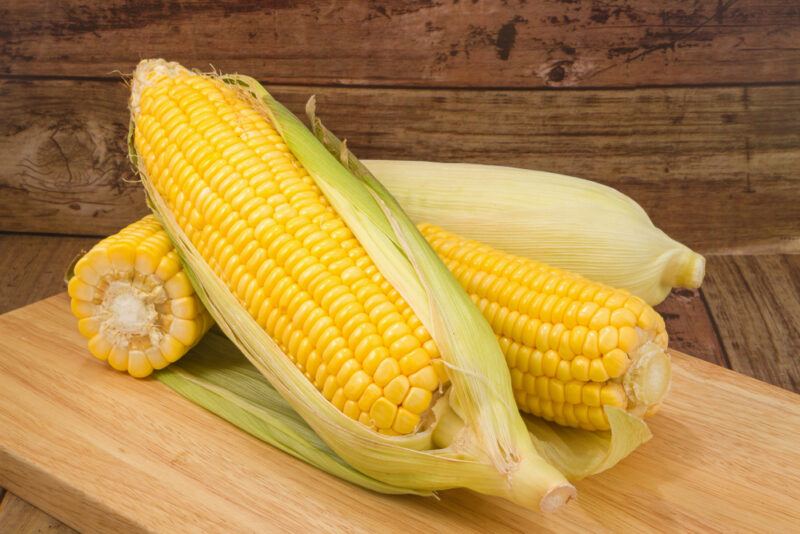 on a wooden chopping board are four fresh yellow corn