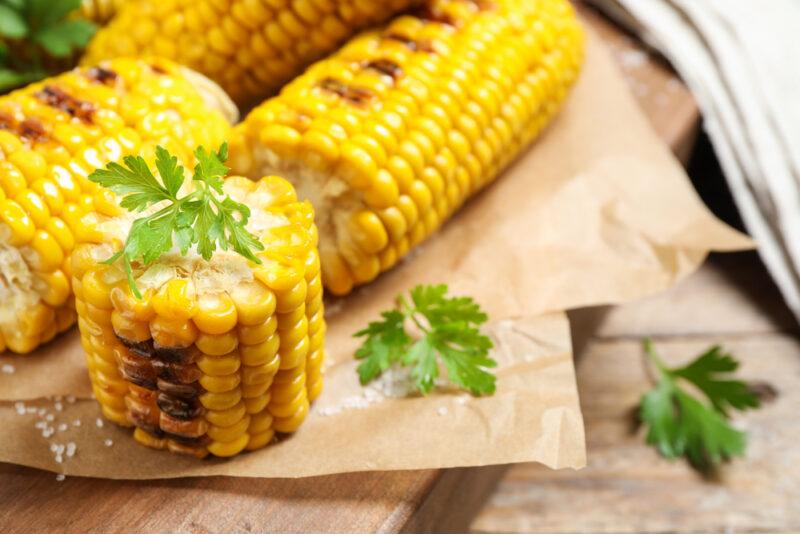 grilled corn on the cobs on brown paper with cilantro herbs and rock salt