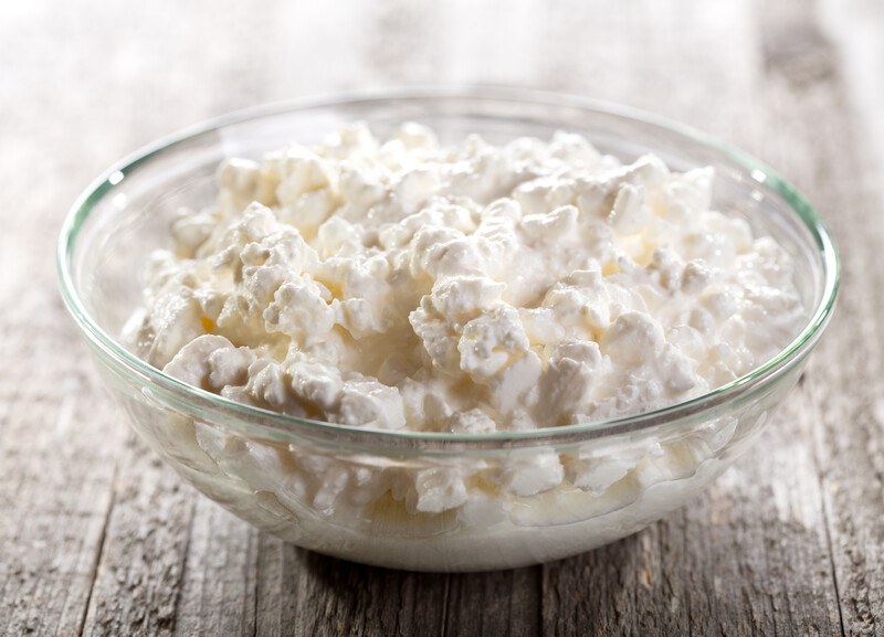 on a wooden surface is a clear glass bowl full of cottage cheese