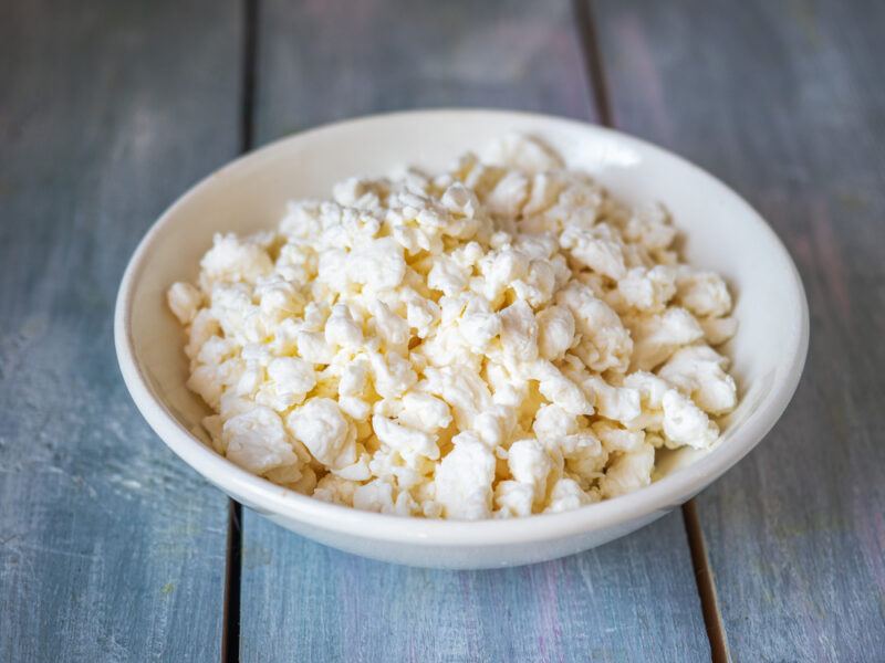 on an aged wooden surface is a shallow white bowl full of cottage cheese