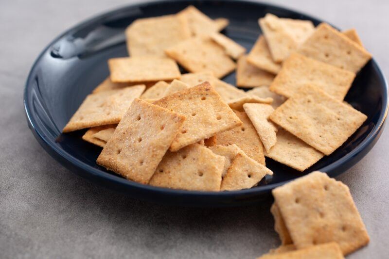 on a concrete surface is a black plate with crackers, beside it is a couple of loose crackers