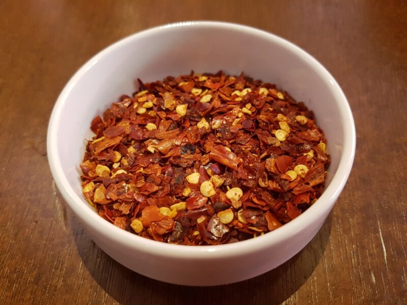 on wooden surface is a white ceramic bowl with crushed red pepper