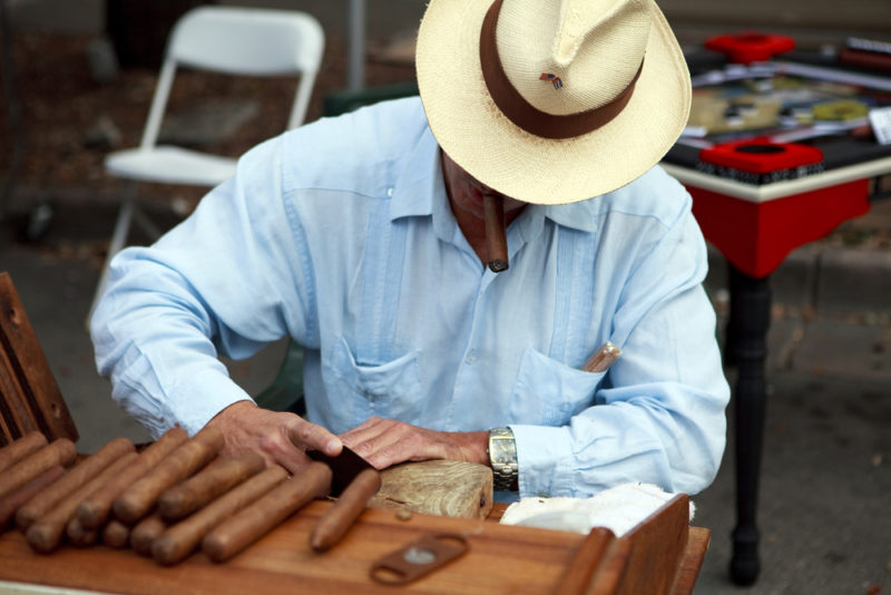 cuban man smoking cigar and hand cutting cigar leaves