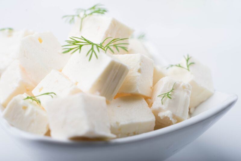 a closeup image of a white bowl full of cubed feta cheese with herbs on top